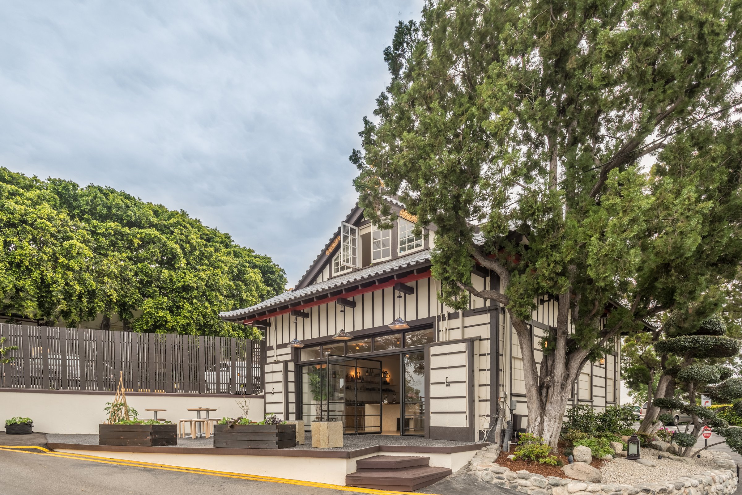 Timber-framed restaurant exterior with open glass doors, a small patio and mature trees.