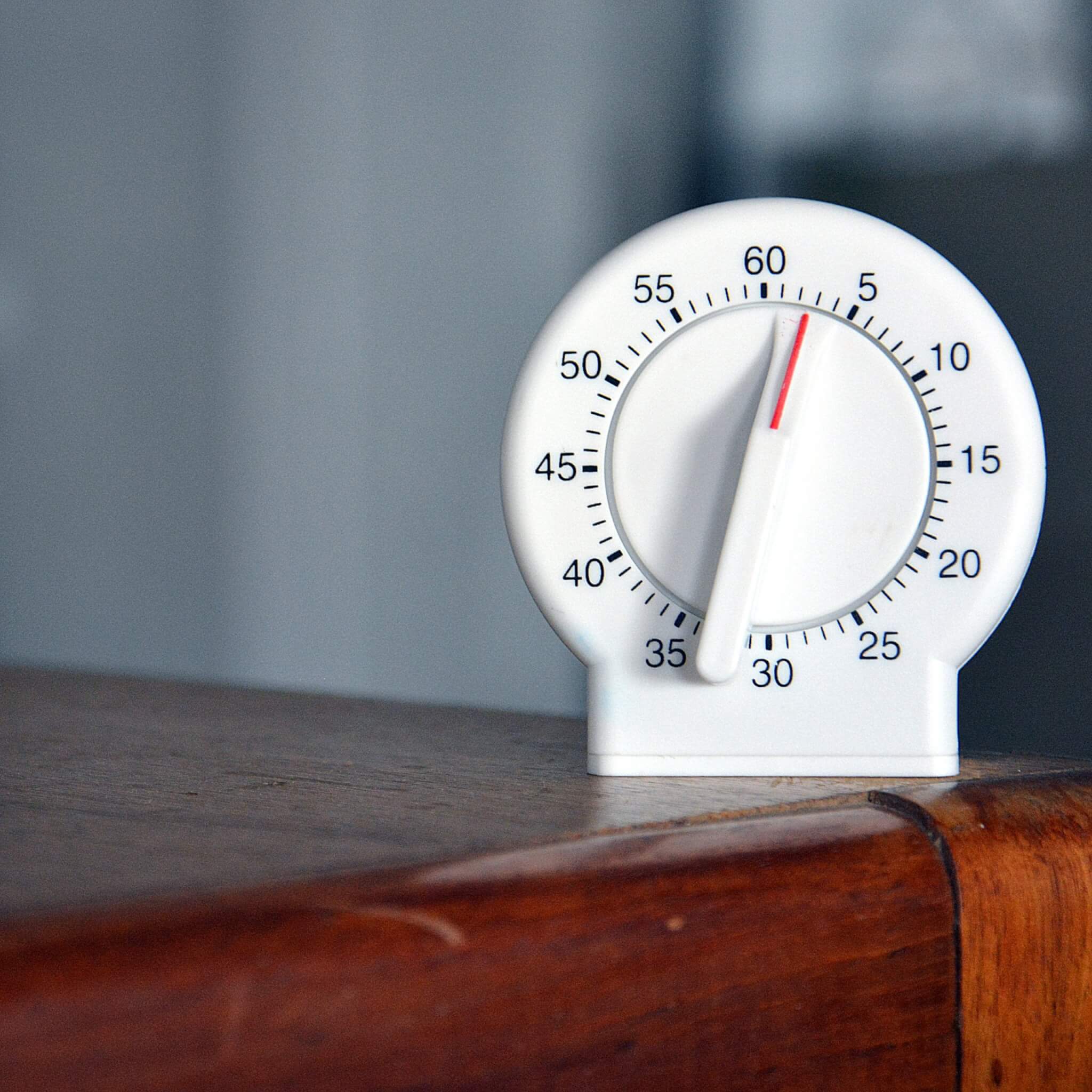White kitchen timer on a wooden desk illustrating timeboxing for remote work productivity