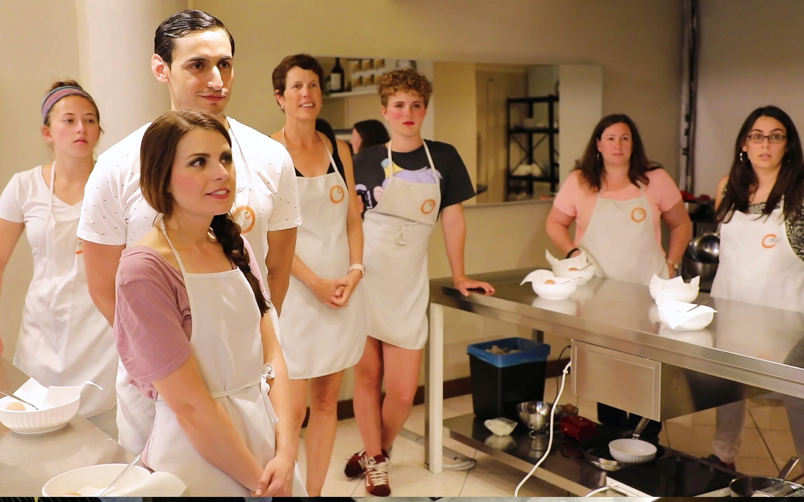 Liten gruppe på et kjøkken i Firenze under en matlagingskurs, iført forklær og lytter oppmerksomt.