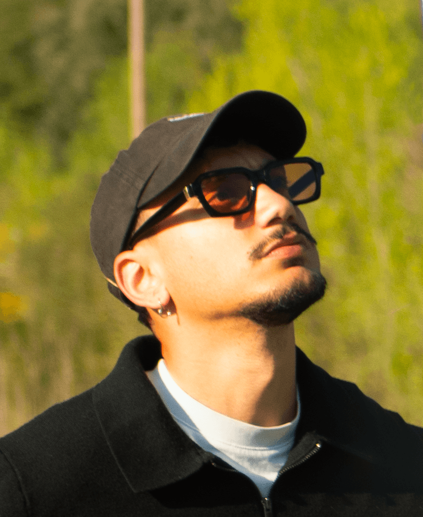 Man sitting in a dimly lit room, wearing a beige shirt and looking contemplative.