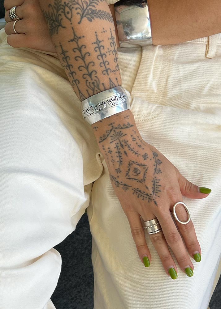 Person's arm with tattoos wearing silver bracelets and rings on a white background