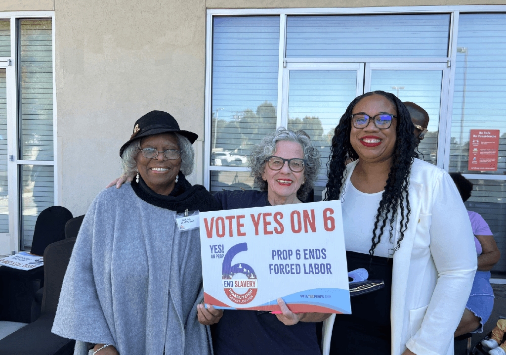 Three women smile while holding a sign that reads “VOTE YES ON 6 – Prop 6 Ends Forced Labor.”