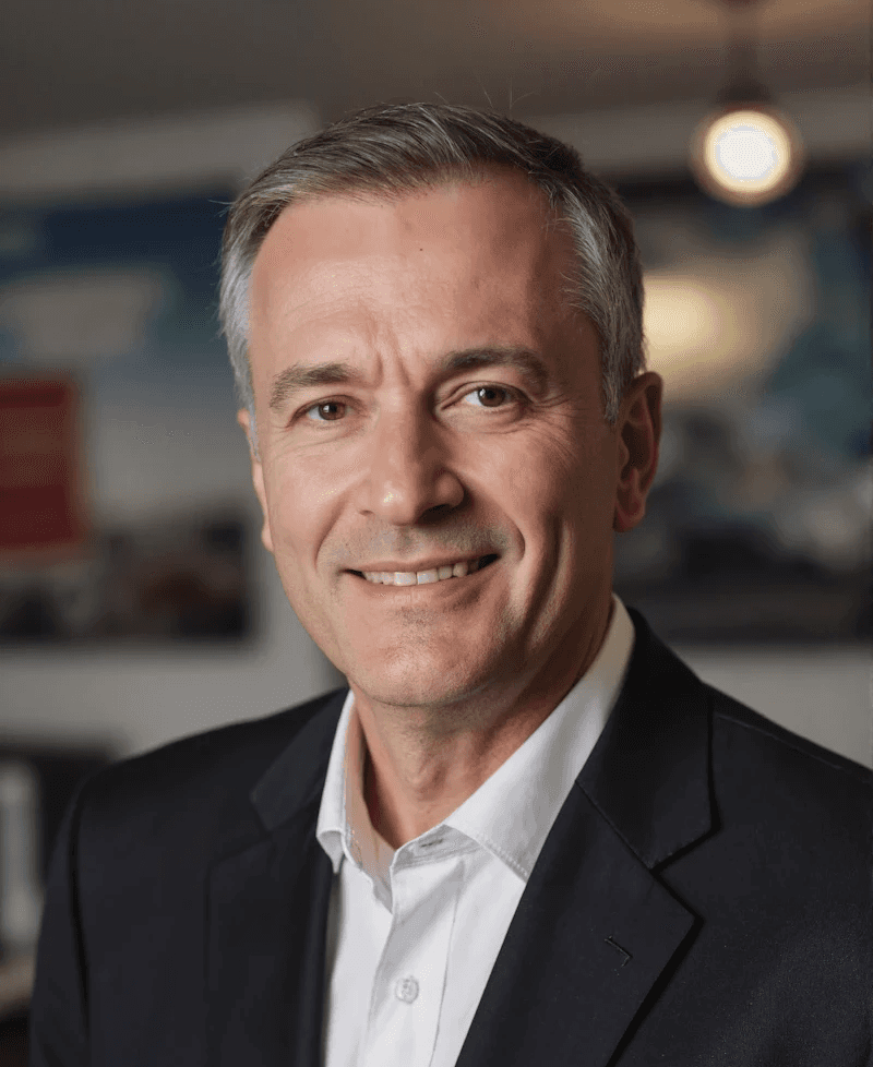 Professional portrait of a middle-aged man in a suit, smiling warmly with a blurred background for a polished, approachable look.