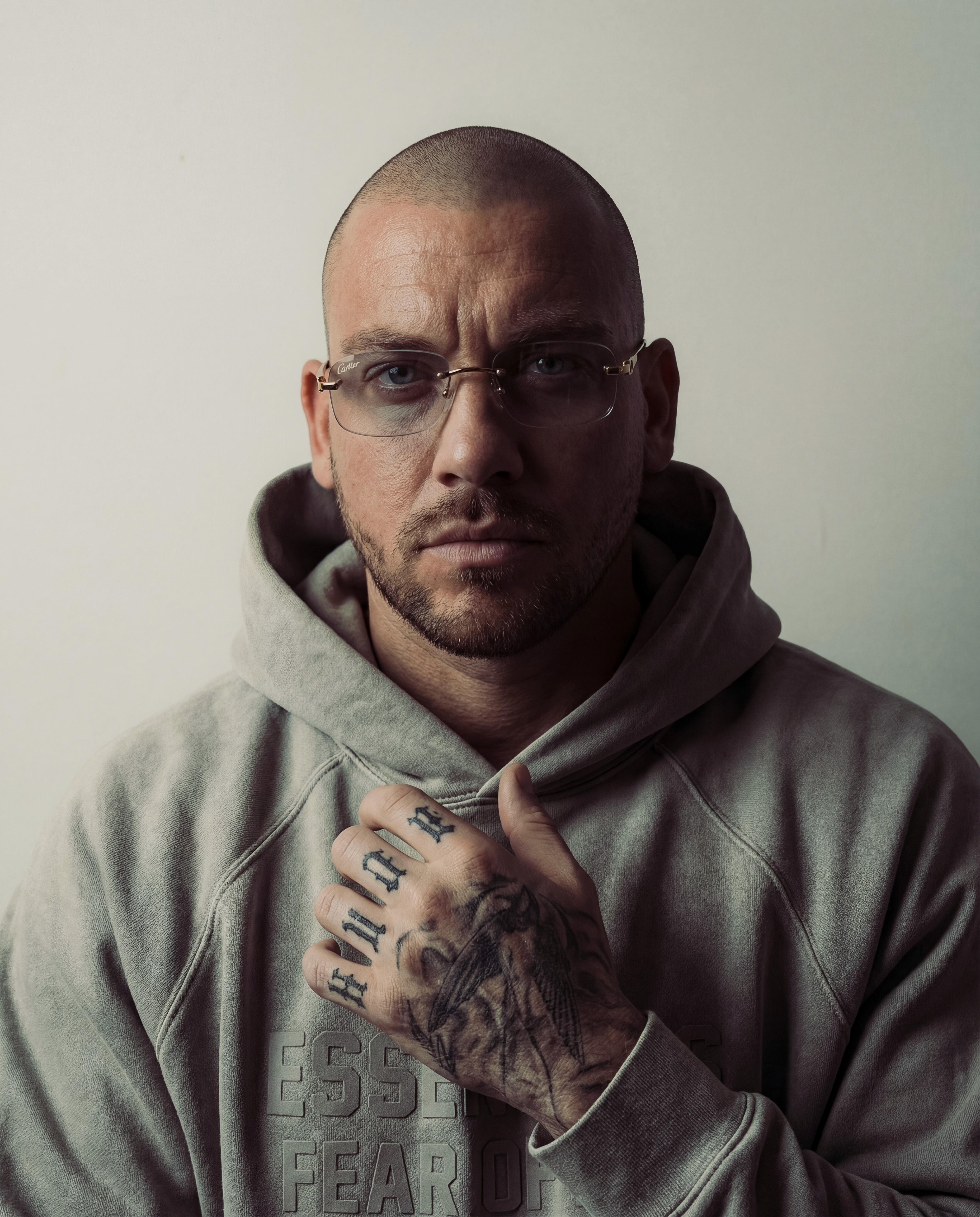 Close-up portrait of a person wearing a gray insulated hooded jacket with the hood up, showing their face framed by the hood against a light background.