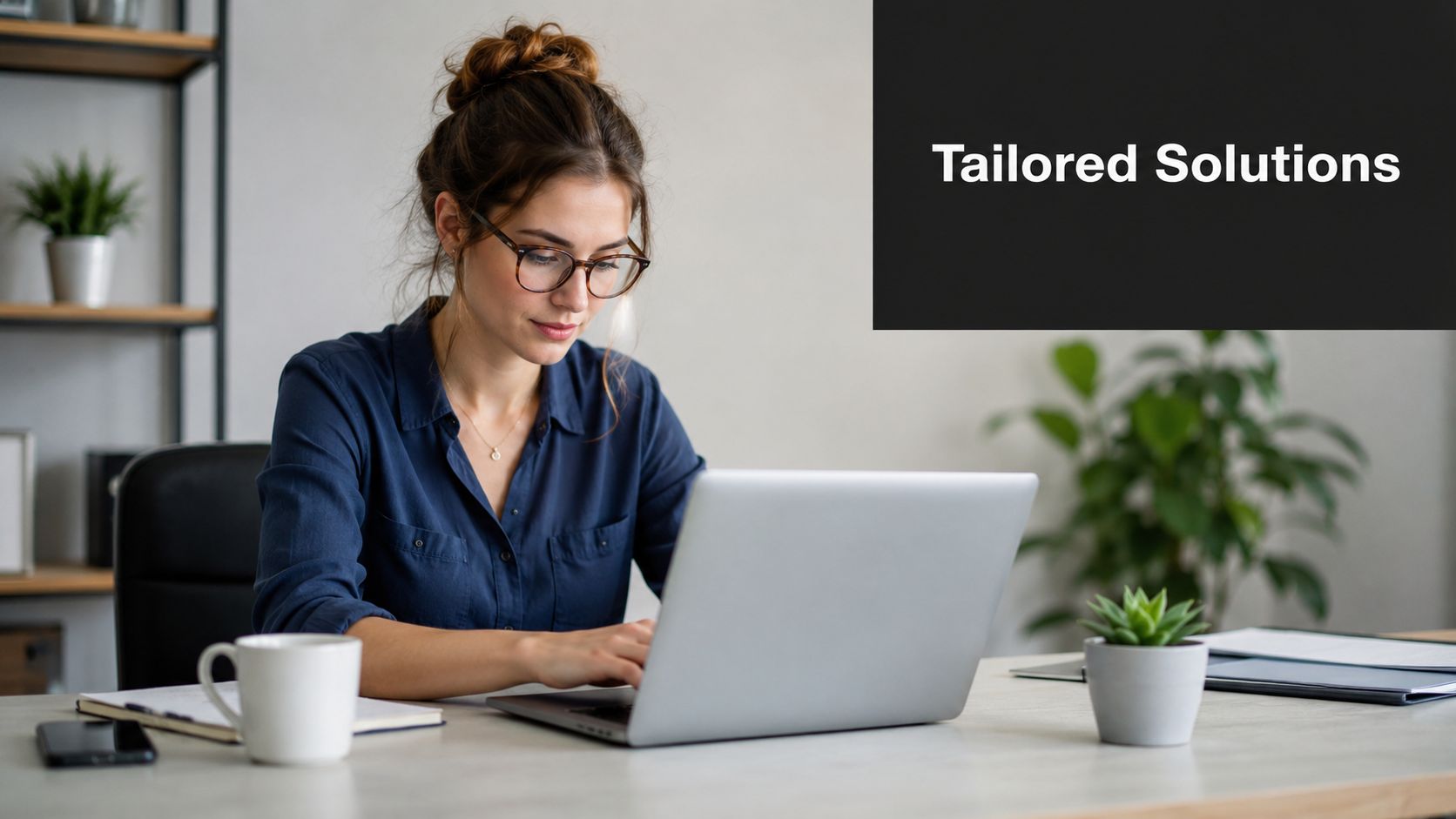 A professional woman working on a laptop at her desk with the text Tailored Solutions displayed.
