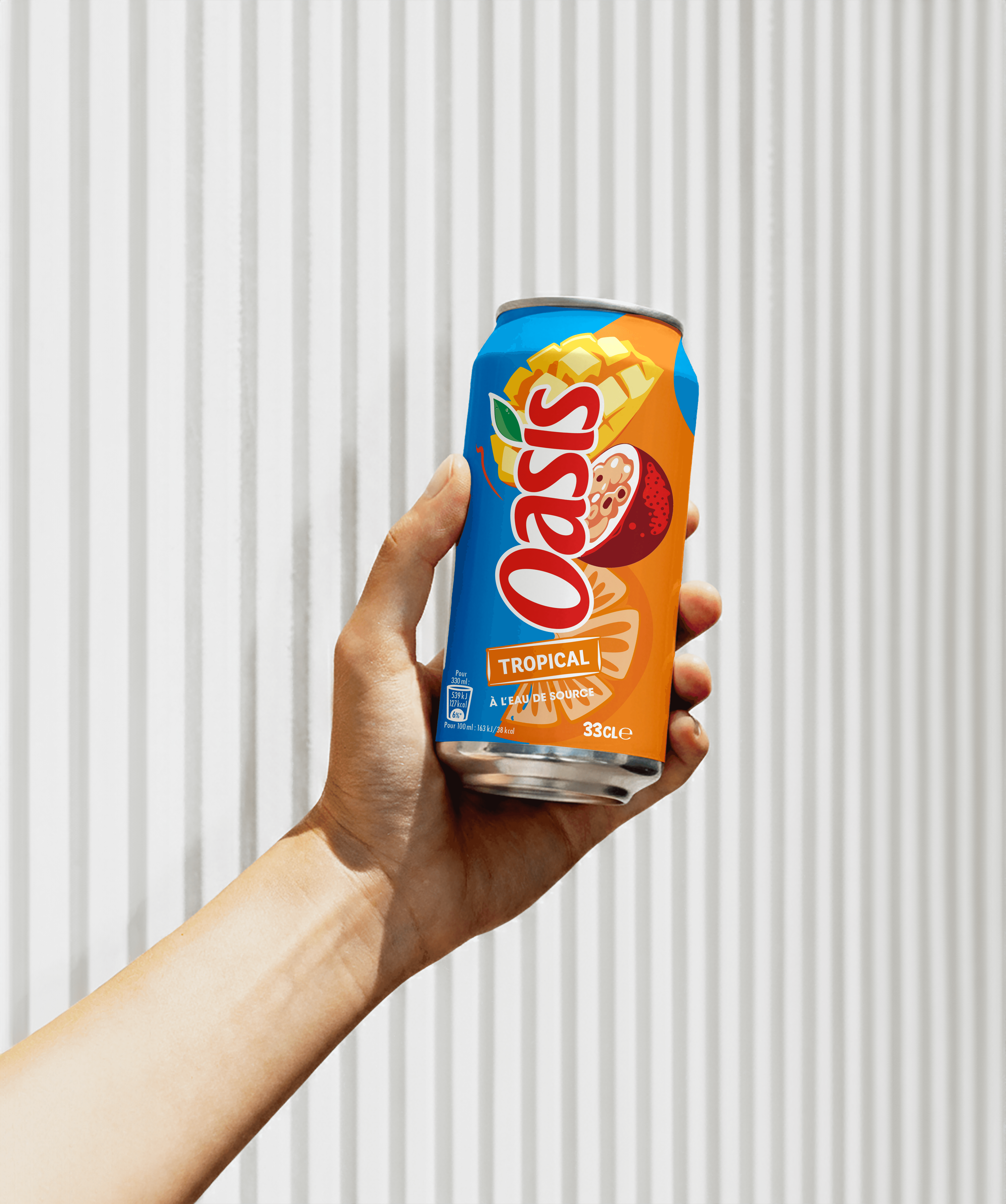 A hand holding a colorful Oasis Tropical soda can against a minimalist, textured white background.