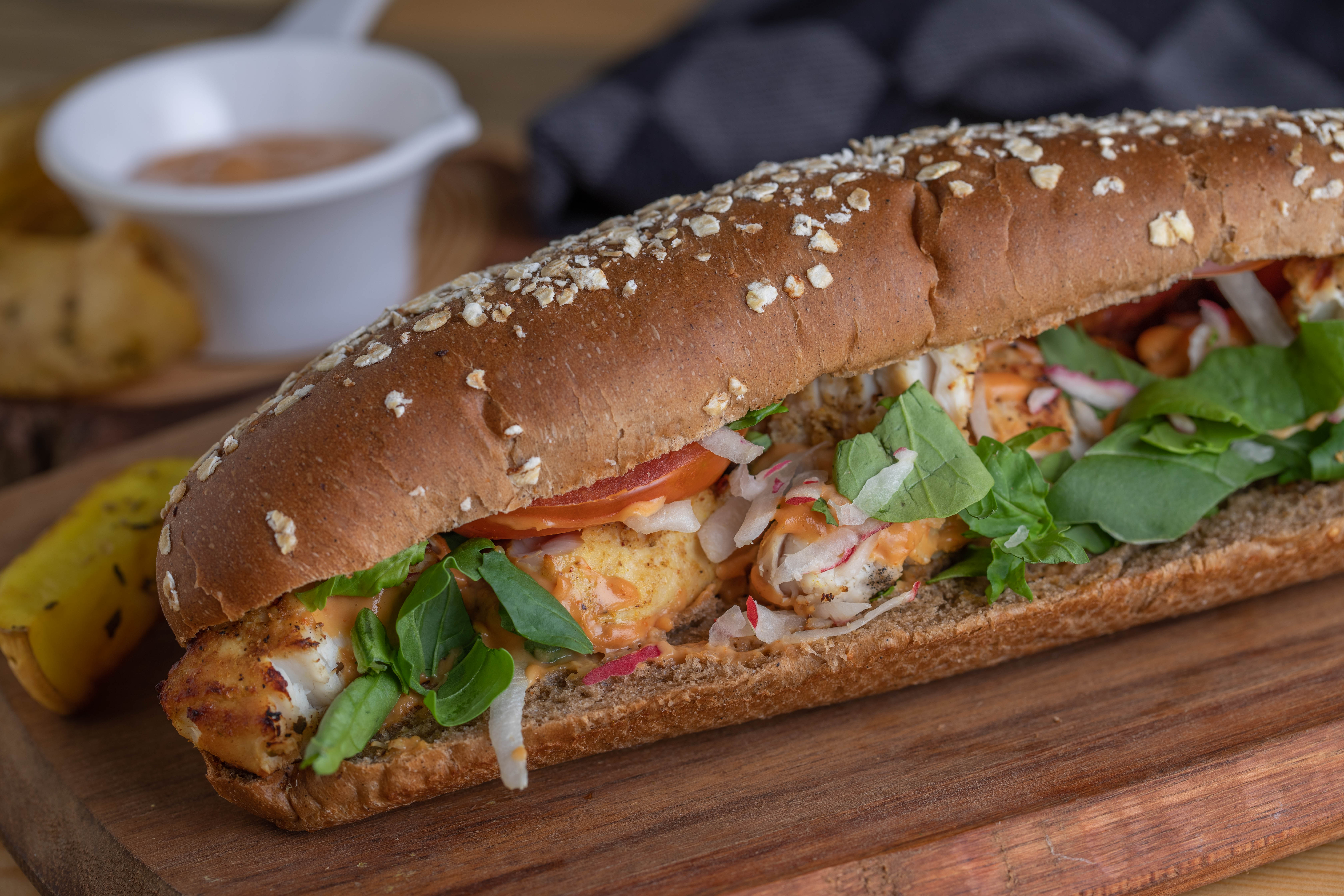 Two people serving food from wooden platters at an outdoor dining setup. A table is set with a white tablecloth.