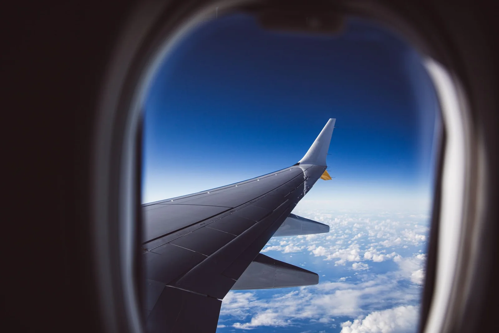 A plain airplane wing above scattered clouds and deep blue sky.