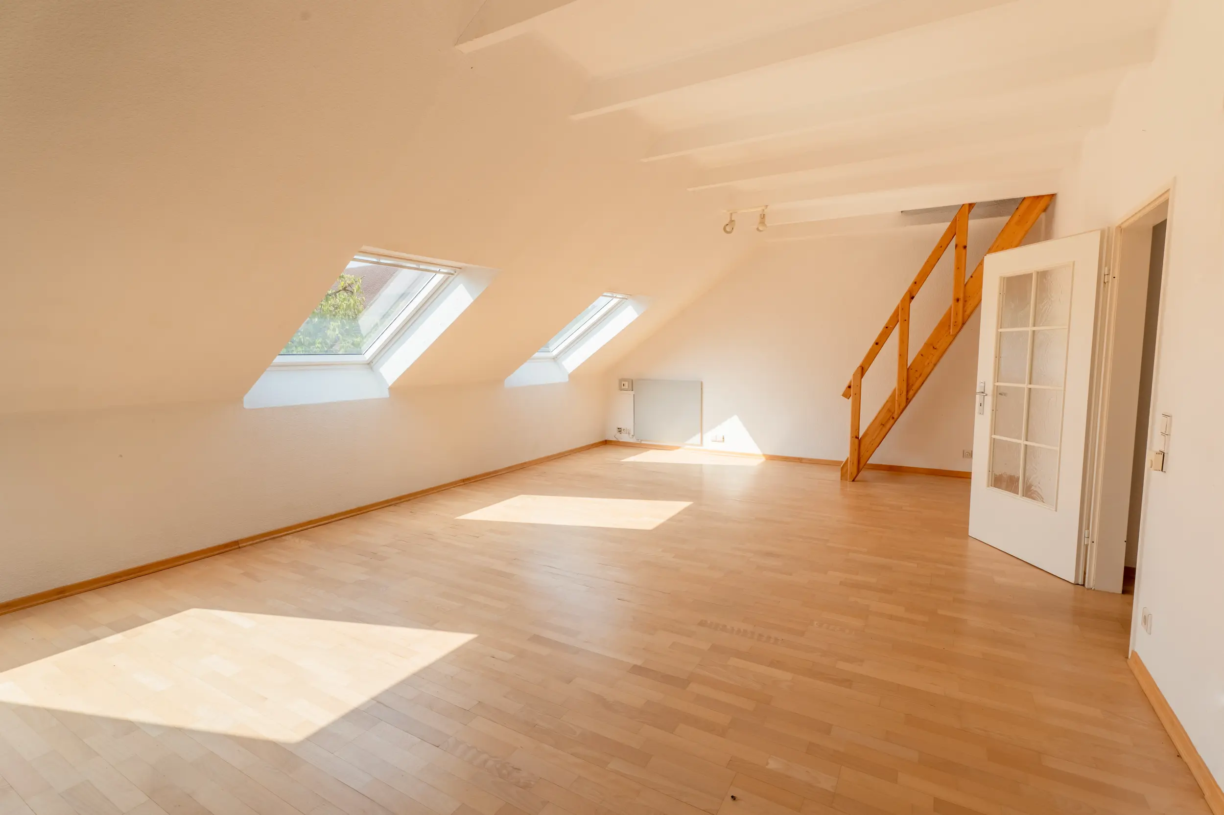 Helles Wohnzimmer der 2-Zimmer-Dachgeschosswohnung in Nordhorn-Blanke mit Laminatboden, Dachflächenfenstern, sichtbaren Holzbalken und Holztreppe zum Dachboden.