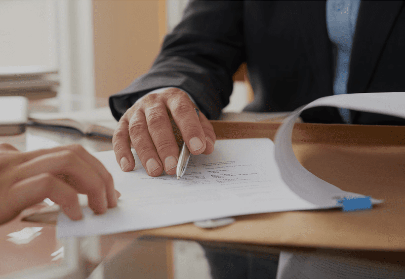 A person wearing a beanie and glasses is working at a computer desk in a sunlit apartment, surrounded by plants, with a cityscape visible through the large windows.
