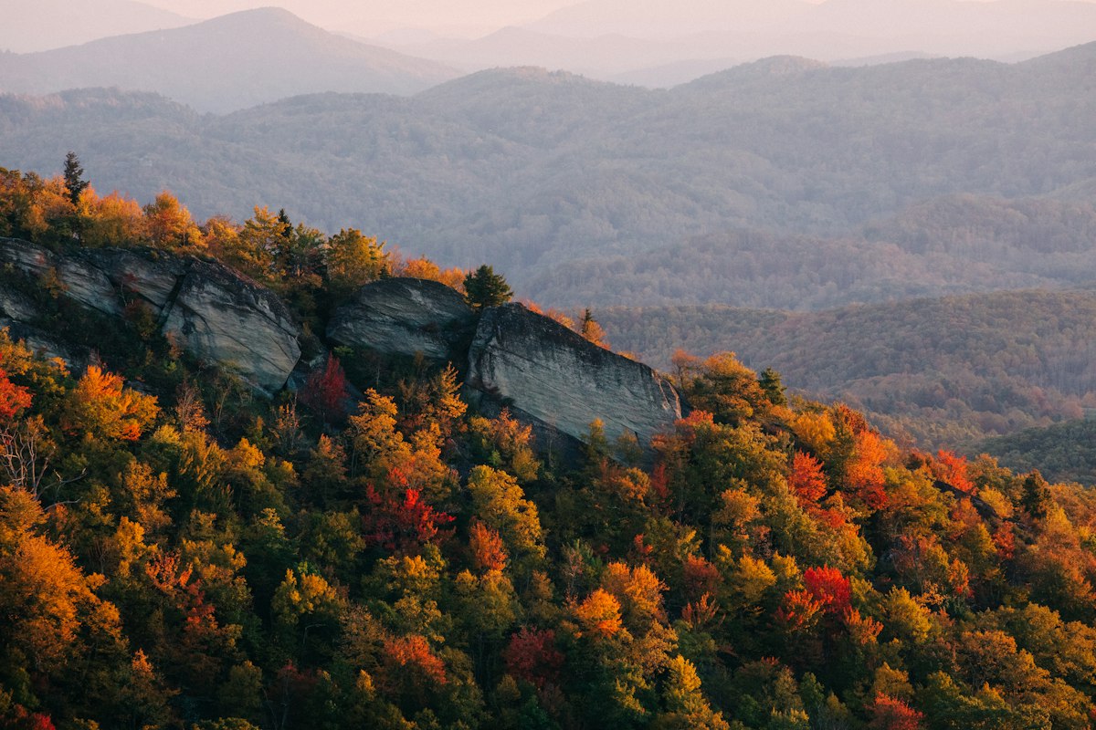 Rocky outcrop above forested slopes with ridges fading into blue haze at peak fall color