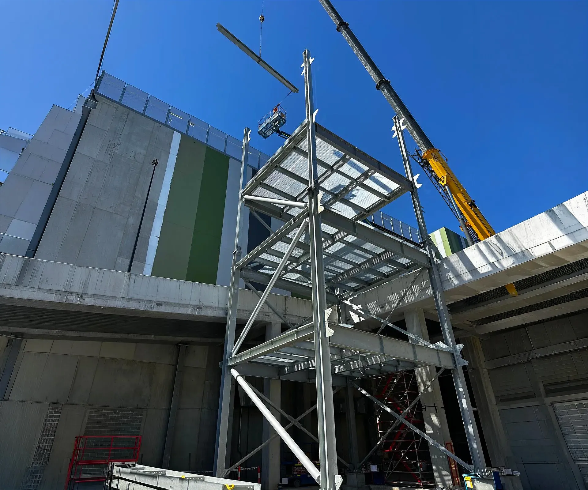Construction of steel frame building with crane and worker in basket.