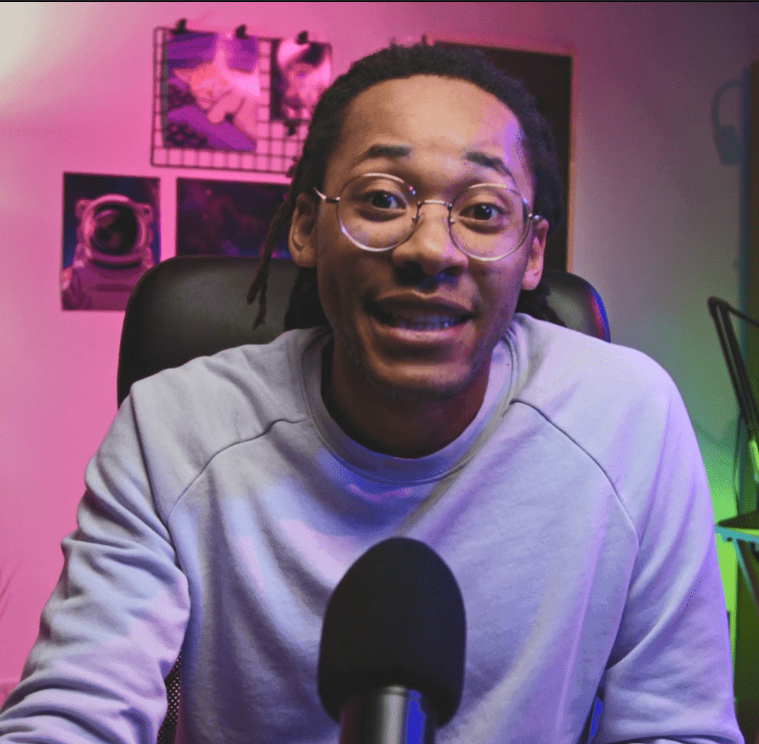 A man wearing glasses speaks into a microphone while sitting in front of a computer.