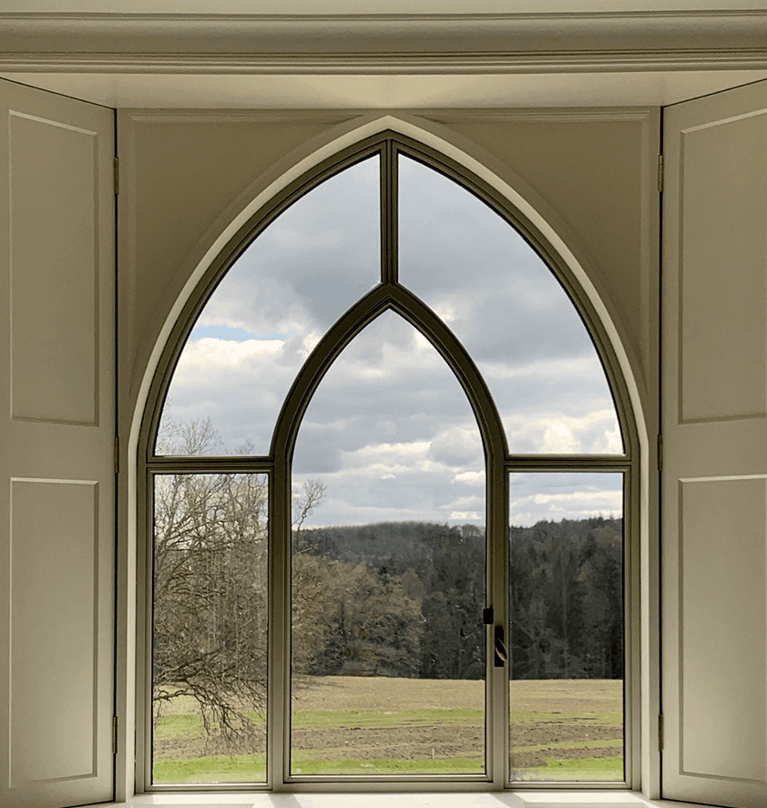 Arched window overlooking a peaceful landscape with fields and cloudy skies.