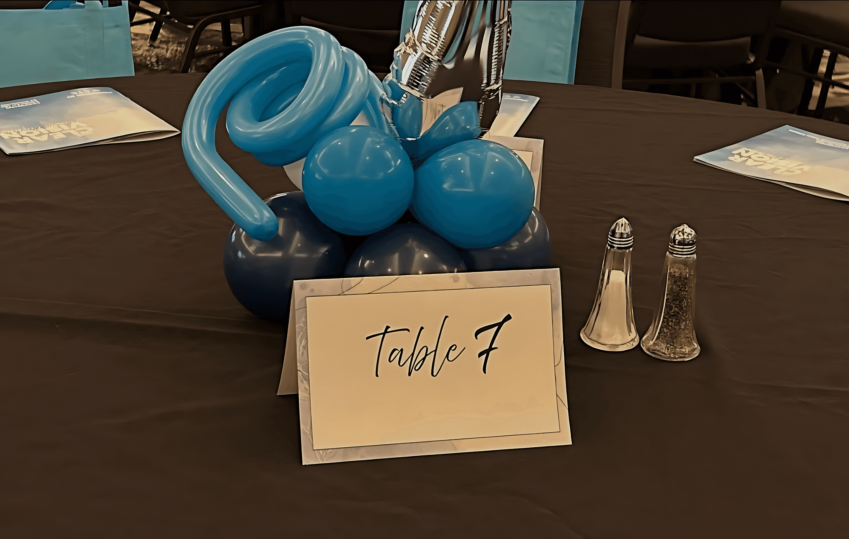 Blue balloon centerpiece next to a table sign labeled Table 7 arranged for an indoor event by Be Bold Balloons