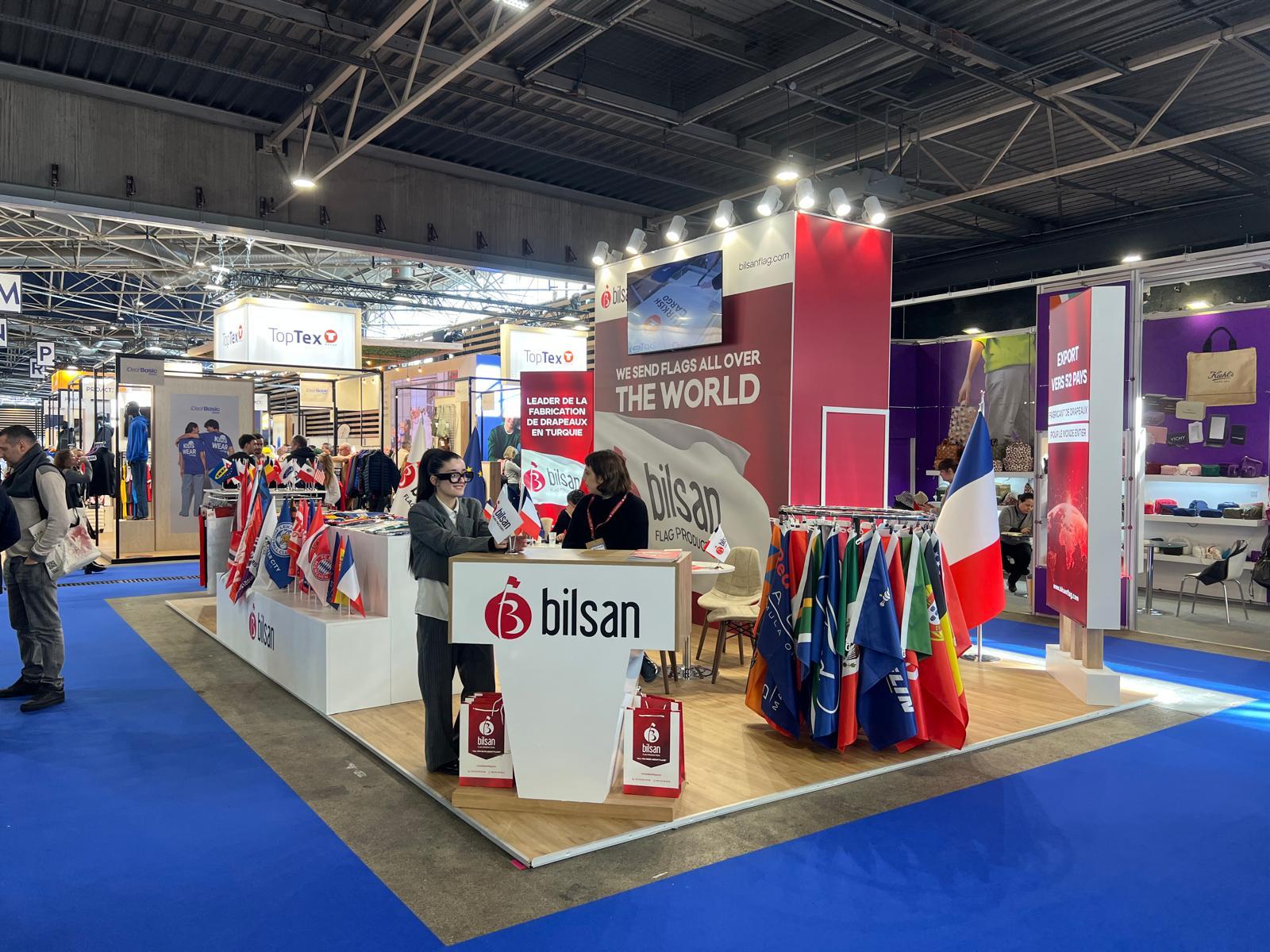 Island layout of the Bilsan stand at CTCO Lyon, allowing visitors to approach from multiple sides with open display counters and flag racks.