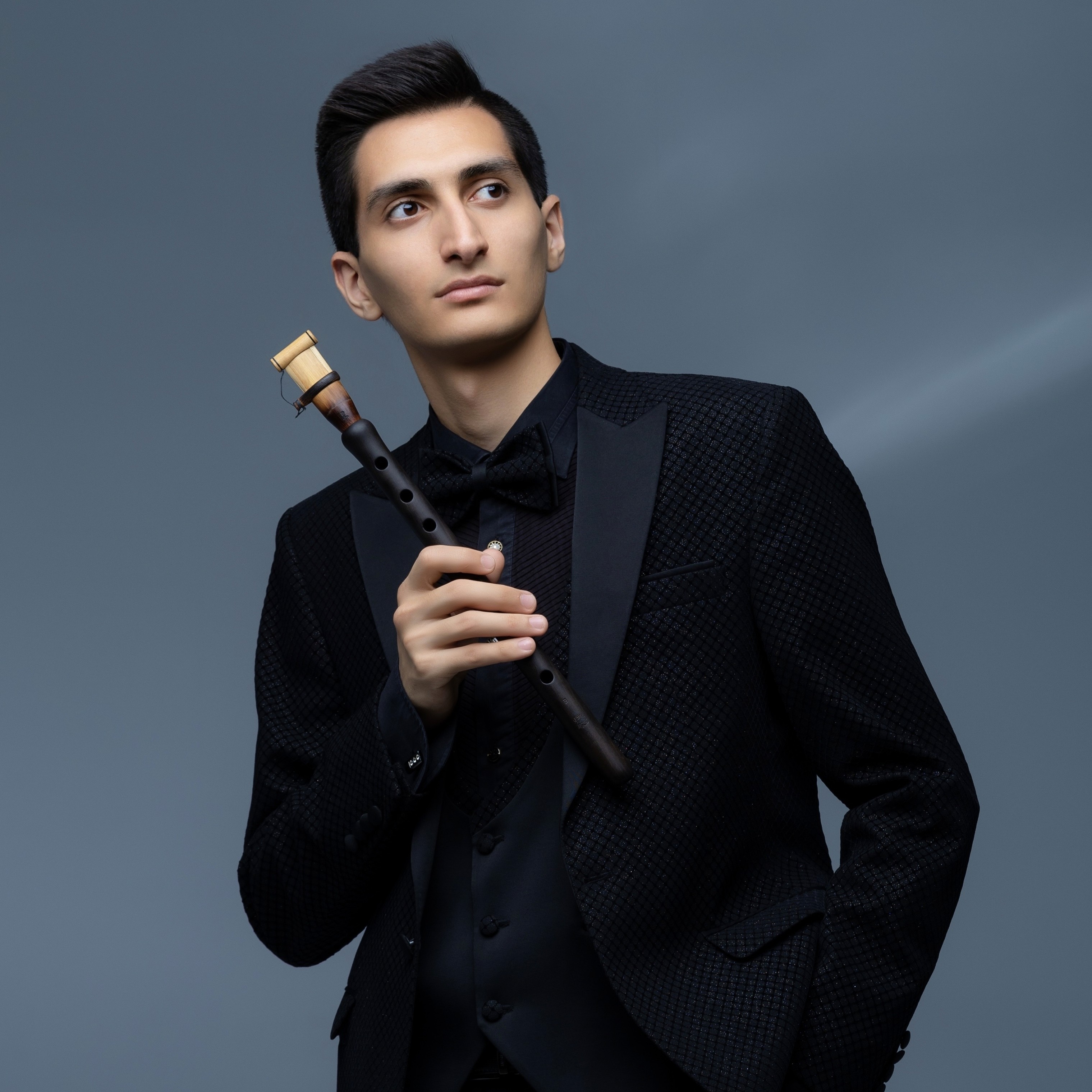 Erik Mirzoyan holding a duduk in a blue-gray studio portrait
