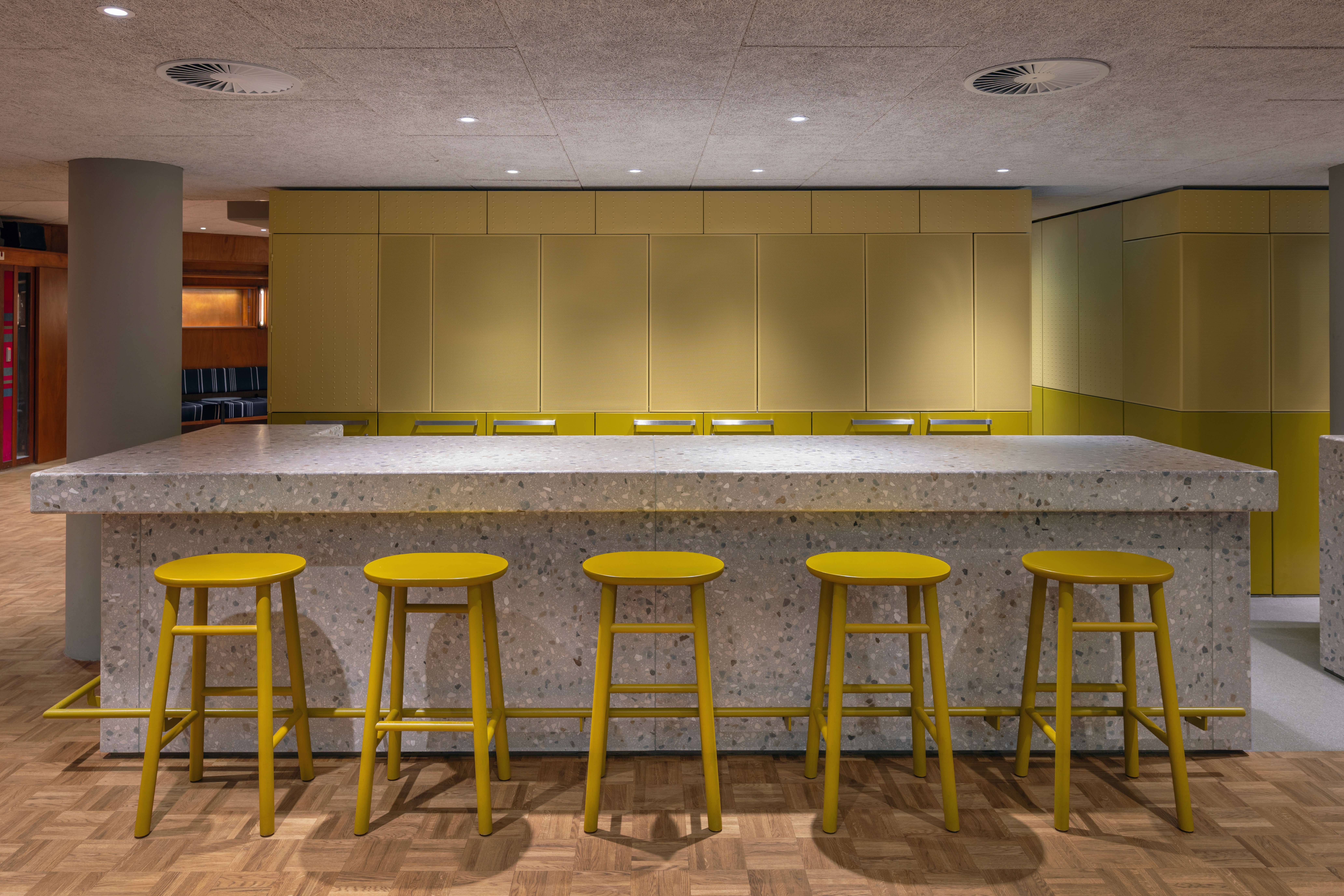 Interieur met terrazzo bar, gele krukken en houten vloer.