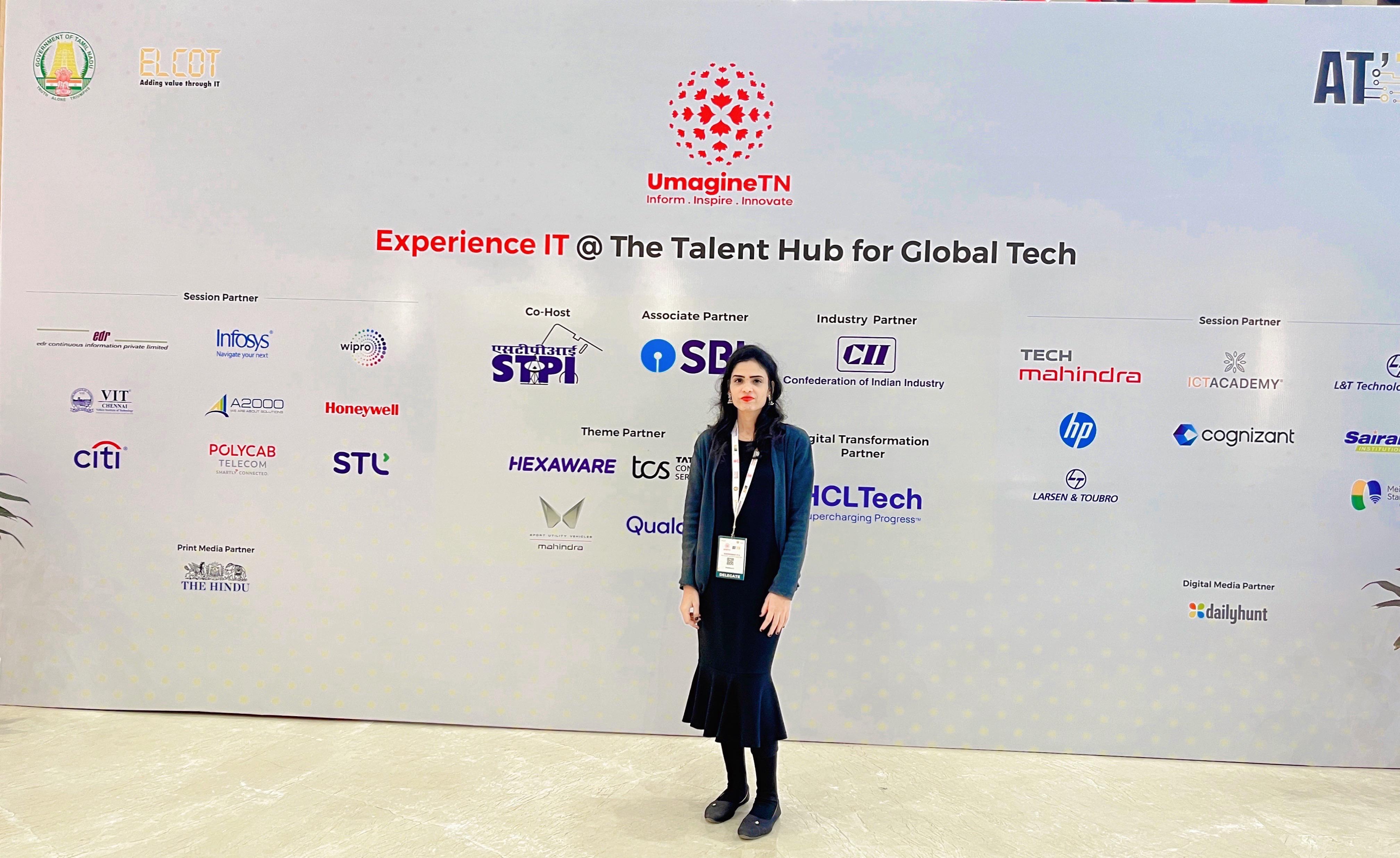 A man stands while two people sit at a table in an office setting, smiling and engaged in conversation. The mood is friendly and collaborative.