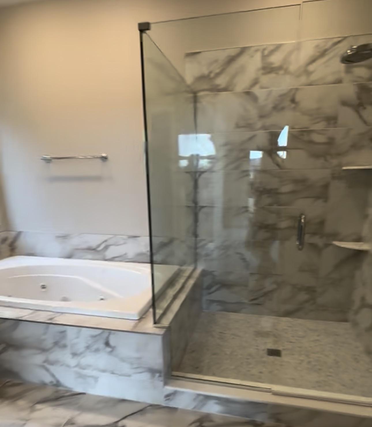 Master bathroom mid-construction with Calacatta marble tile on floor, tub surround, and shower walls — phone photo, not staged