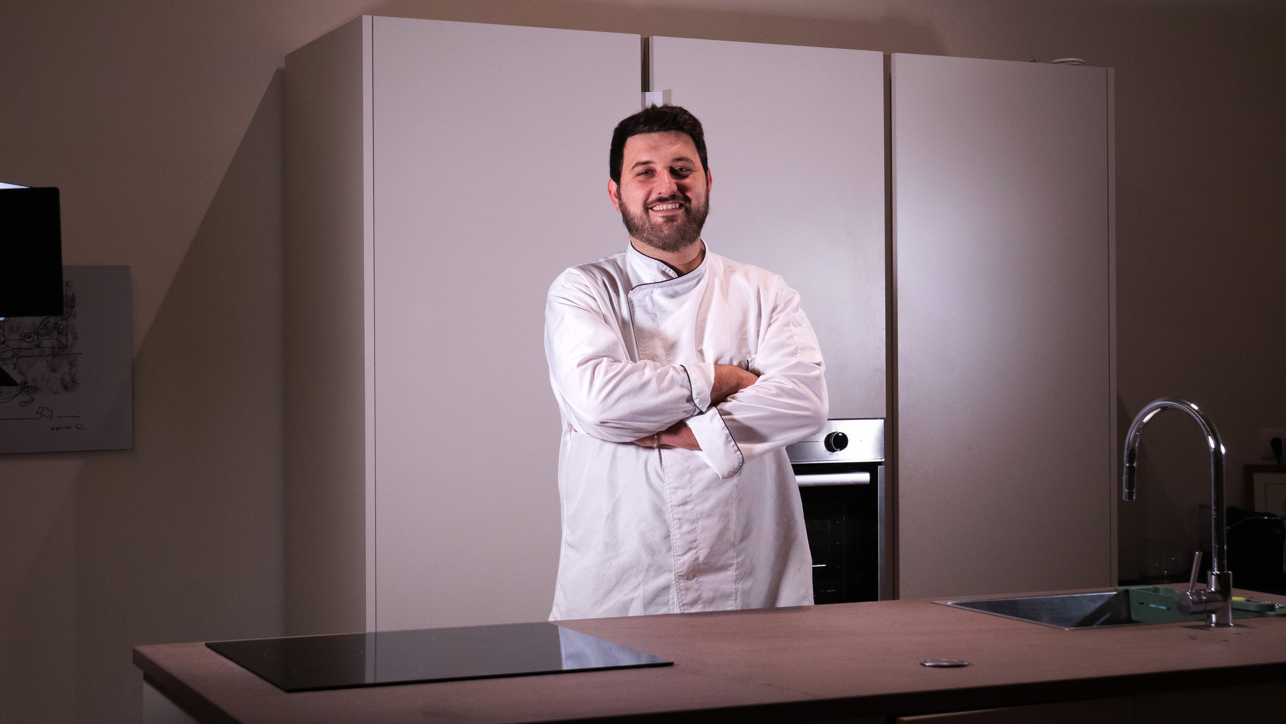 Cozy cafe corner with a round terrazzo table surrounded by wooden chairs, decorated with potted plants and a large mirror reflecting warm light.