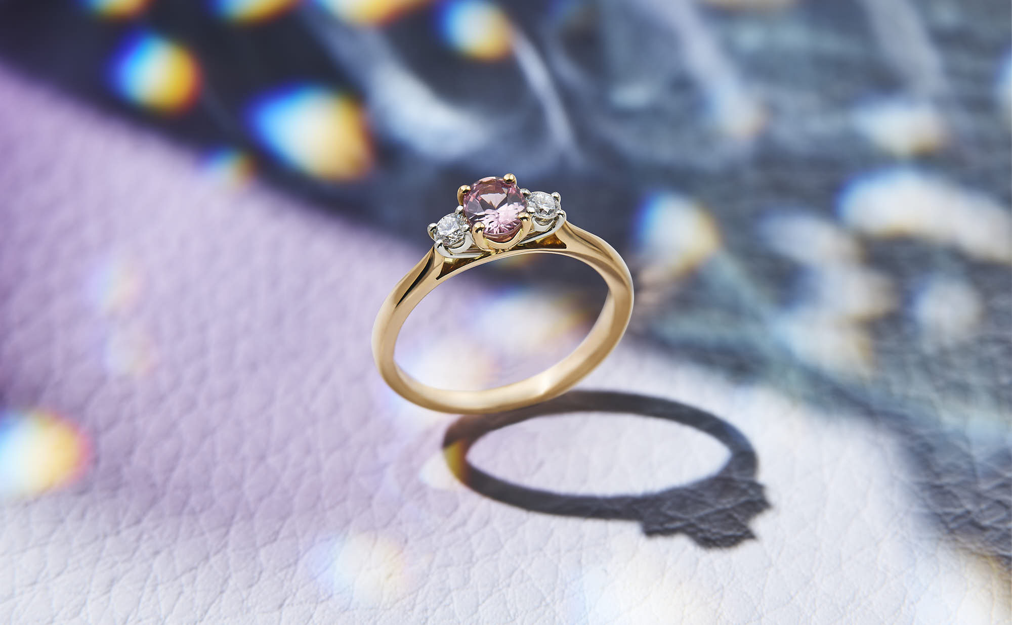 Elegant gold ring with pink gemstone and two diamonds on artistic background.