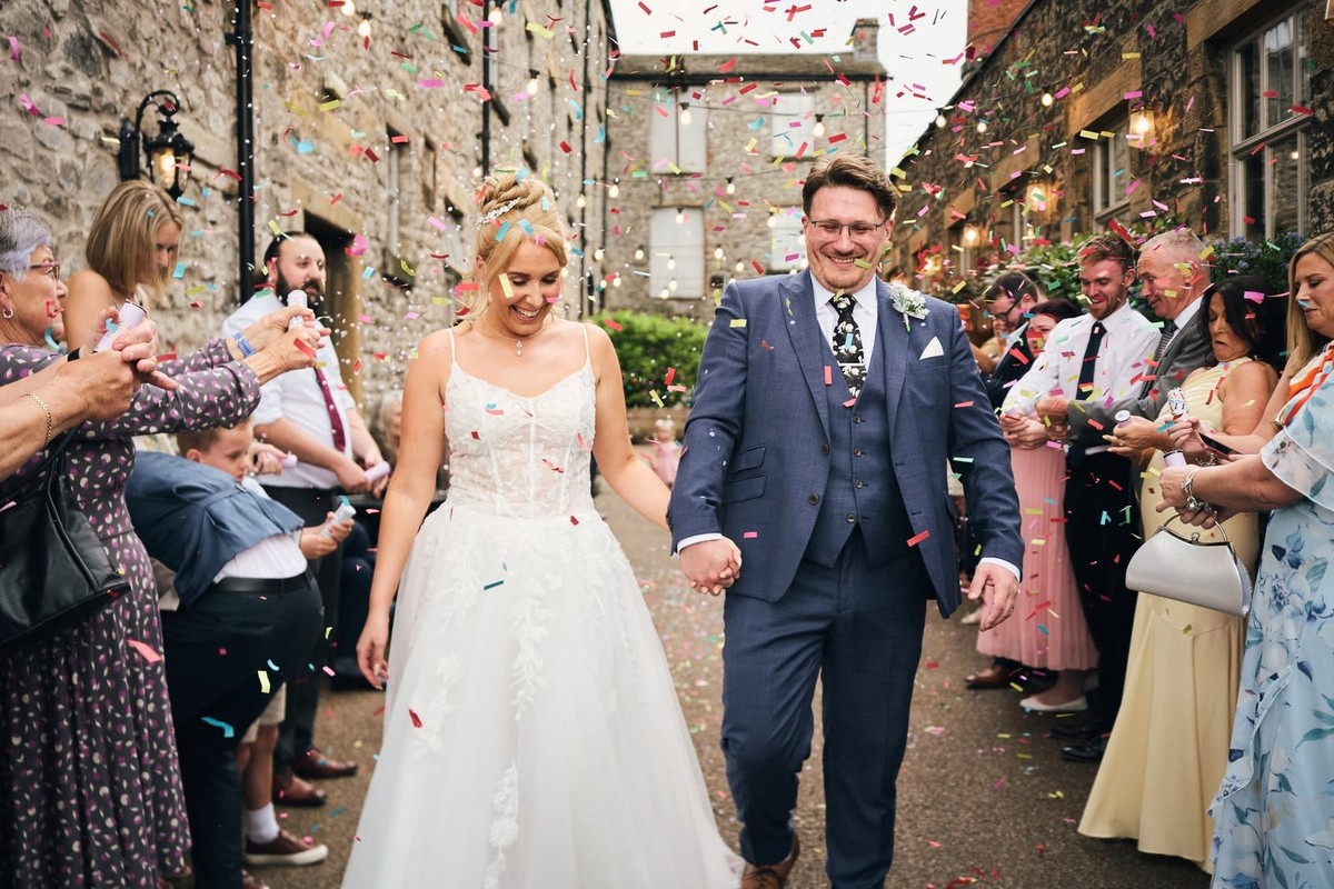 Bride and groom walking hand in hand through guests throwing confetti in the Holmes Mill courtyard