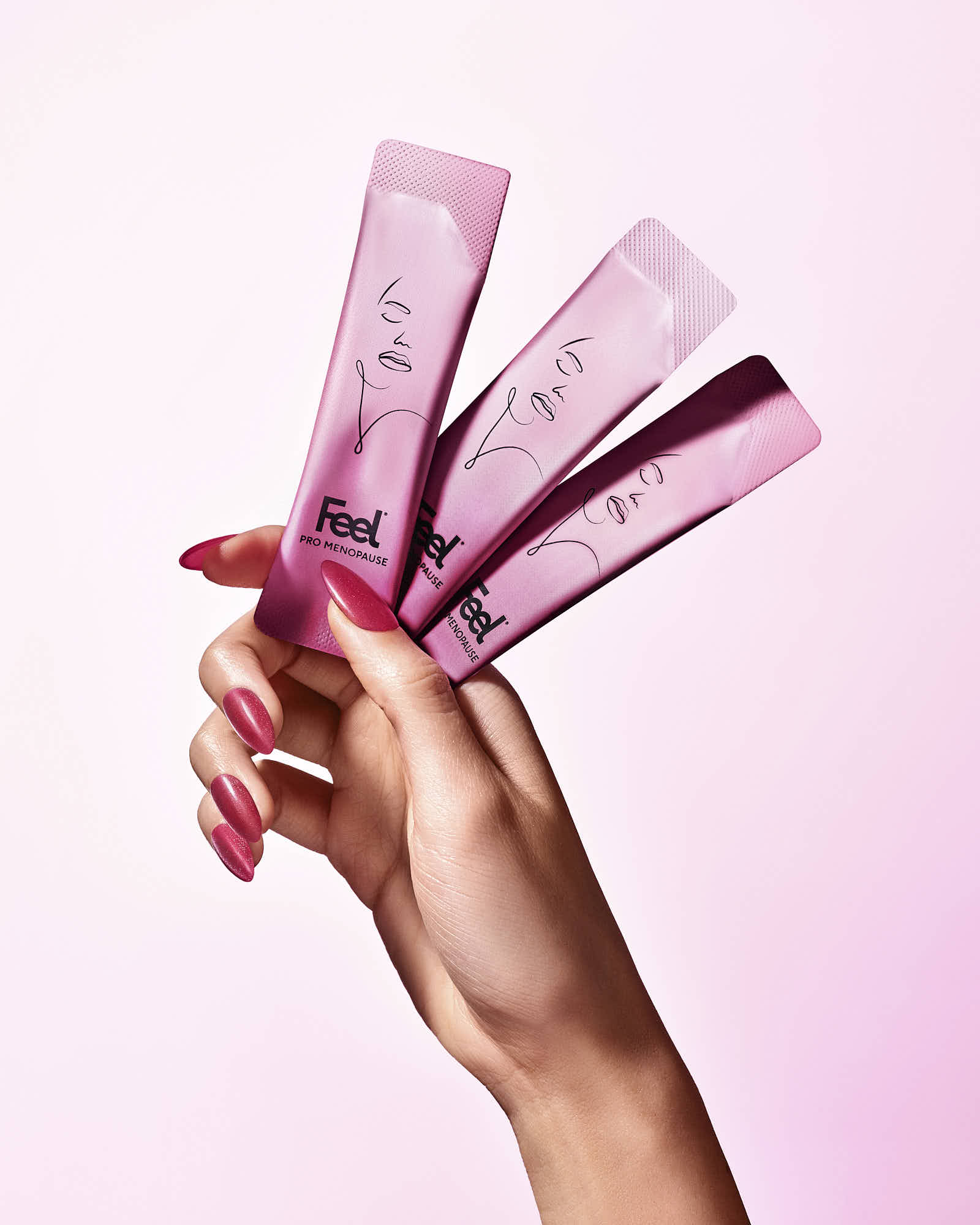 Woman holding pink "Feel" menopause supplements against a pink background.