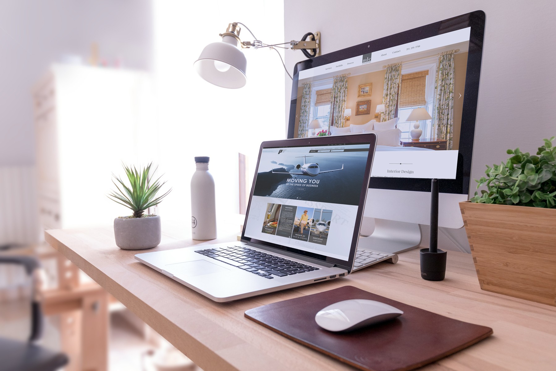 Modern office setup with laptop and desktop showing web design projects, beside a small plant and desk lamp, illustrating a clean, professional digital workspace.