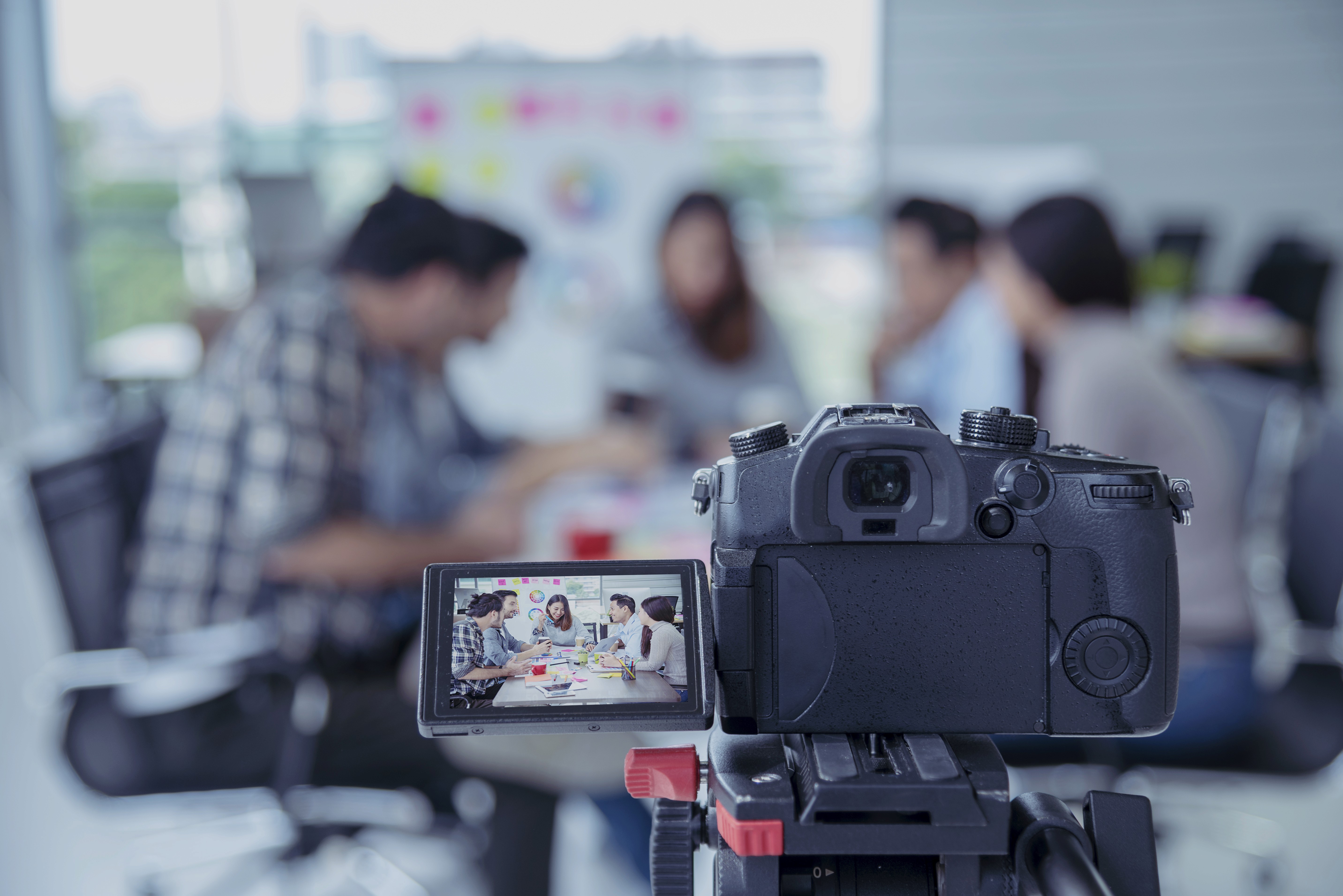 Professional video camera on a tripod filming a team meeting in a modern office, representing the Content Day production model where a videographer captures a full month of video assets in a single structured shoot