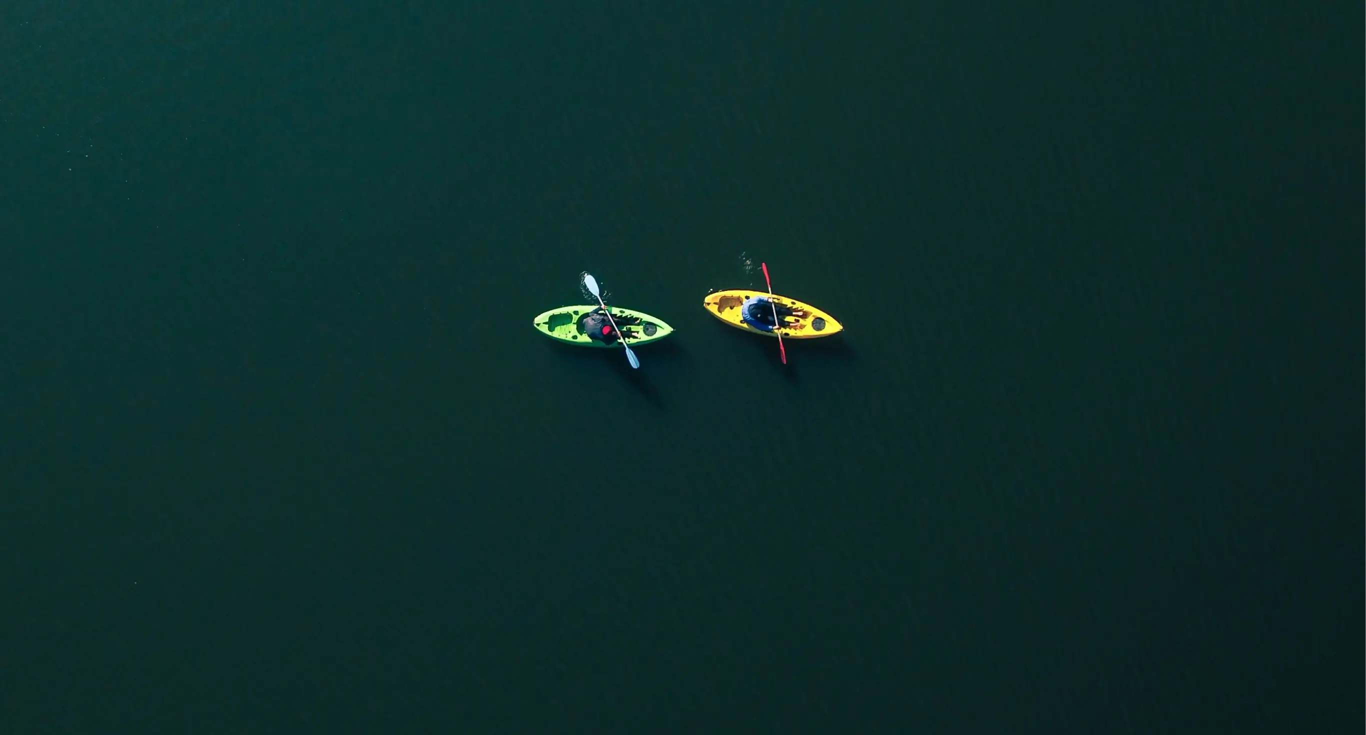 A green lake seen from above with two people rowing in canoes