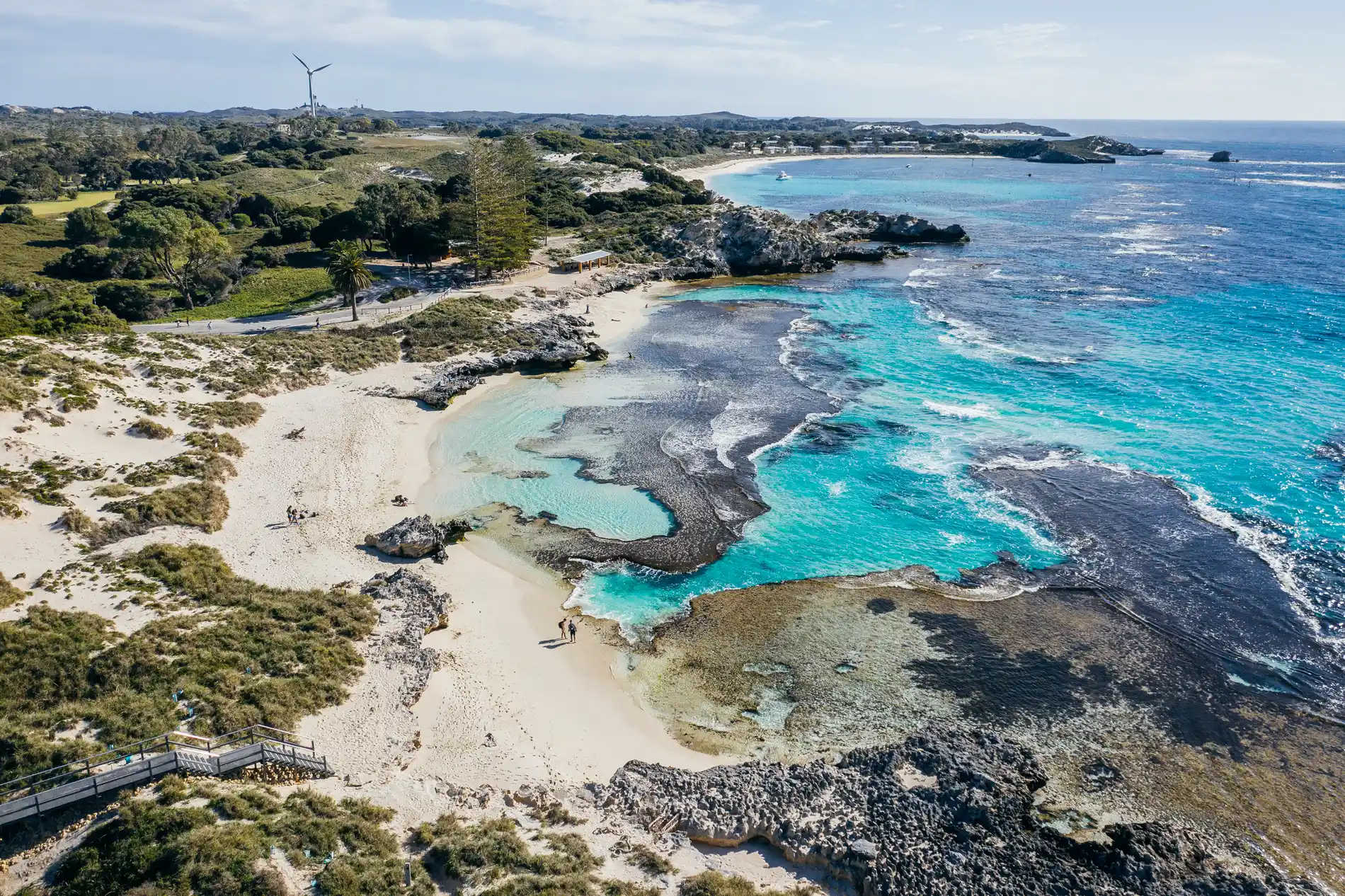 Aerial of a rocky bay with sheltered pools, boardwalk and a wind turbine beyond