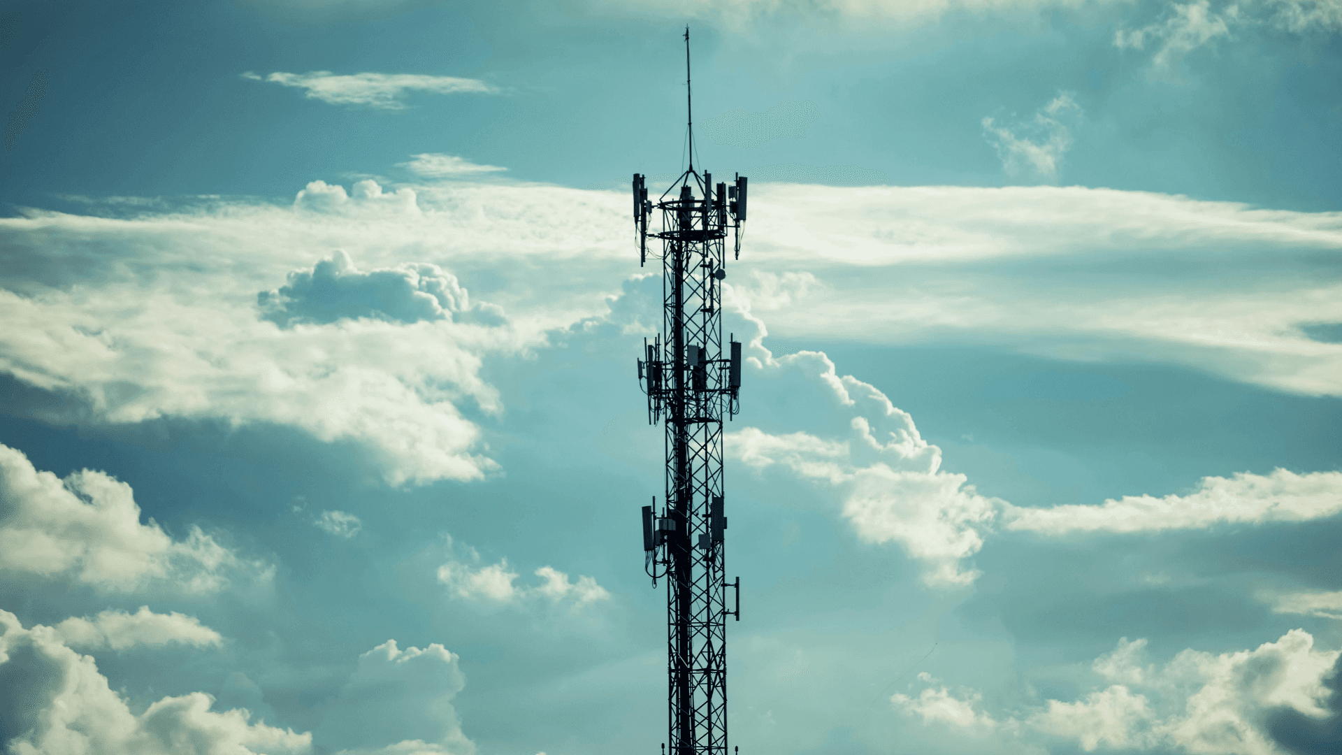Telecommunications cell tower against a cloudy sky, used to represent cellular networks and RF infrastructure.