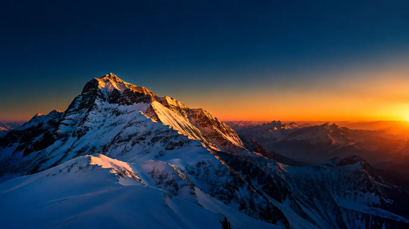Snow-covered alpine peak at golden hour with a deep navy sky transitioning to warm orange horizon light