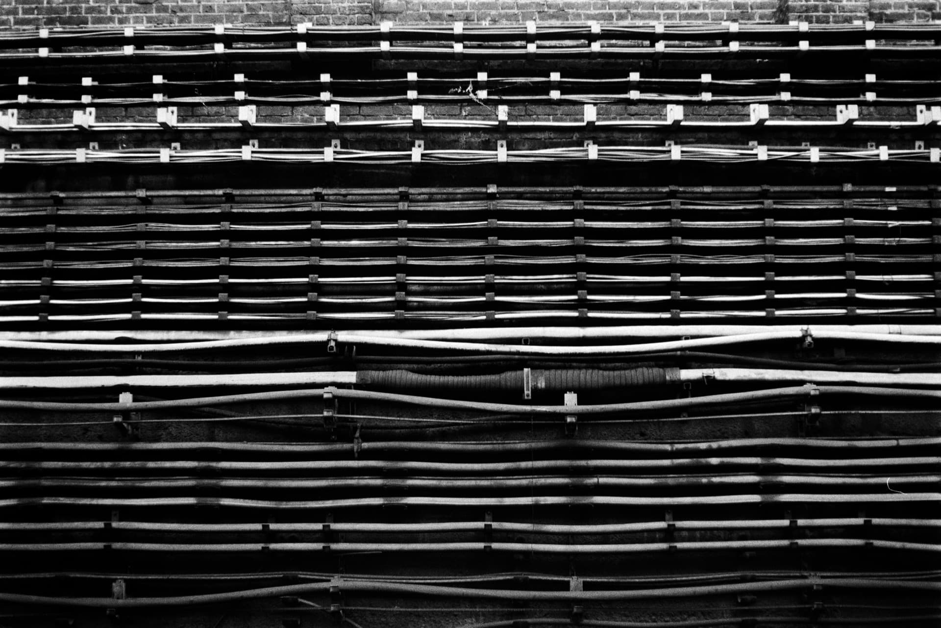 Organized rows of railway cables and mounting brackets on brick wall beside tracks