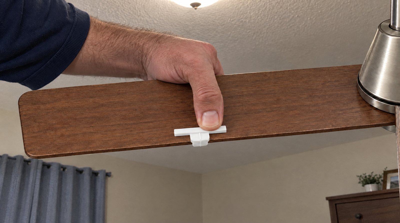 Pressing a small white Barnakl Pearl clip onto the top of a fan blade in the bedroom.