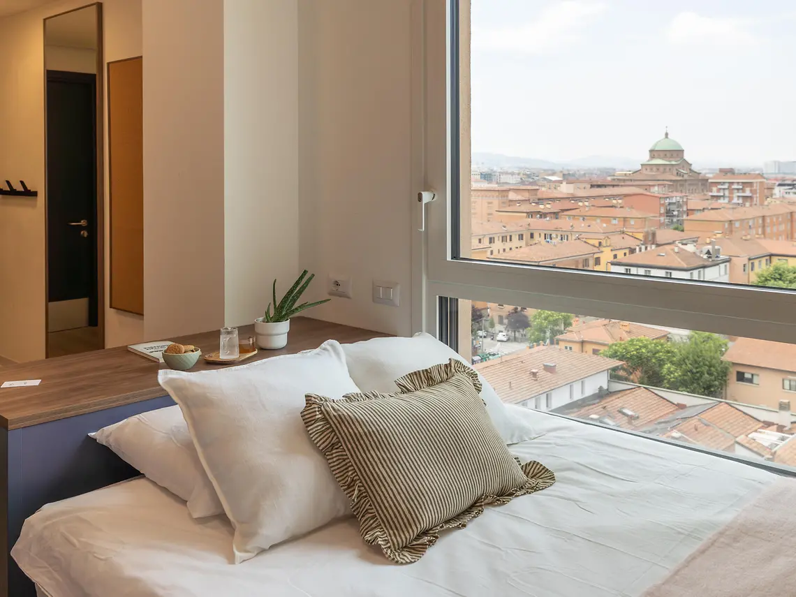 Student studio bedroom with large window and rooftop views over Bologna