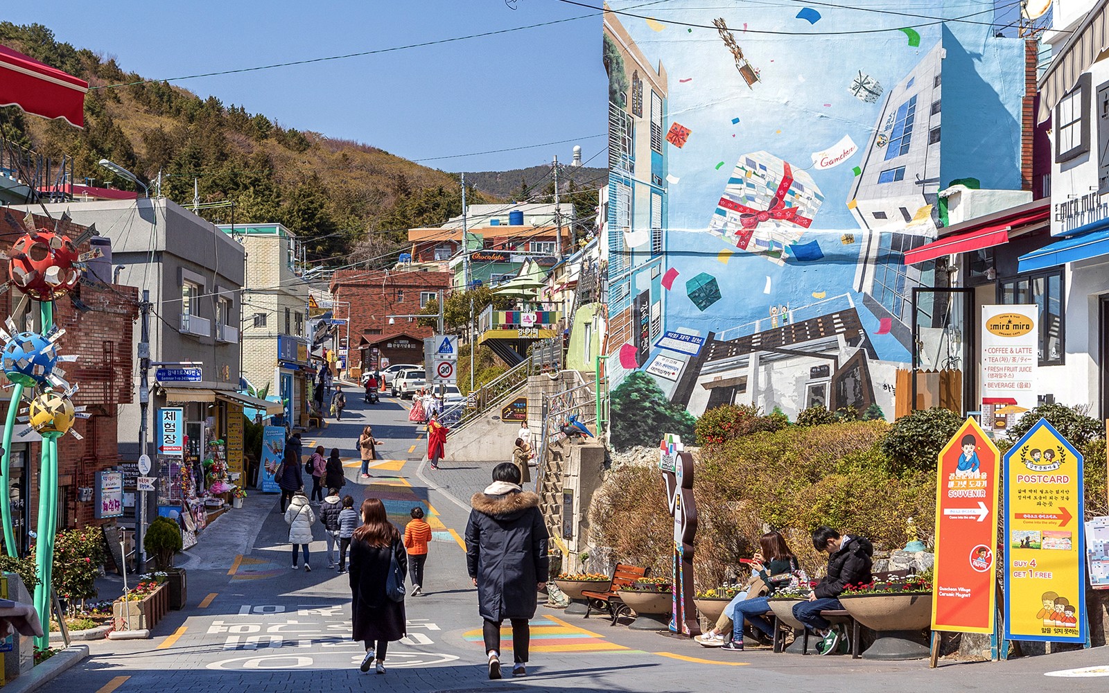 Straßenansicht des Gamcheon Culture Village in Busan mit bunten Wandmalereien und Touristen, die es erkunden.
