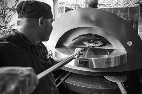 Chef using a peel to slide a pizza into a wood-fired oven.