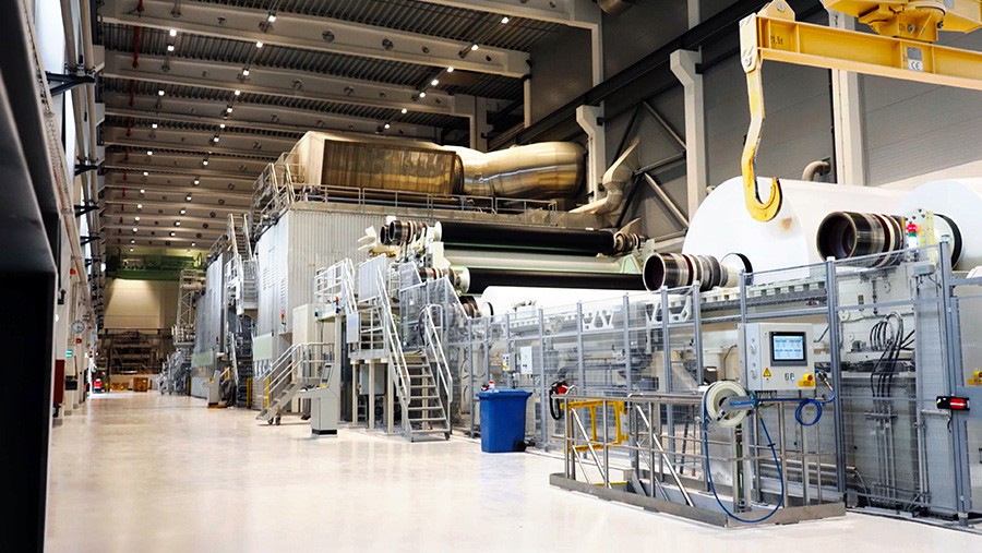 Modern glass and steel building with warm wooden ceilings, surrounded by lush greenery, blending contemporary architecture with nature.