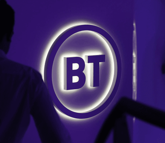 Illuminated BT logo sign with a man standing in front, captured at night in a corporate setting.