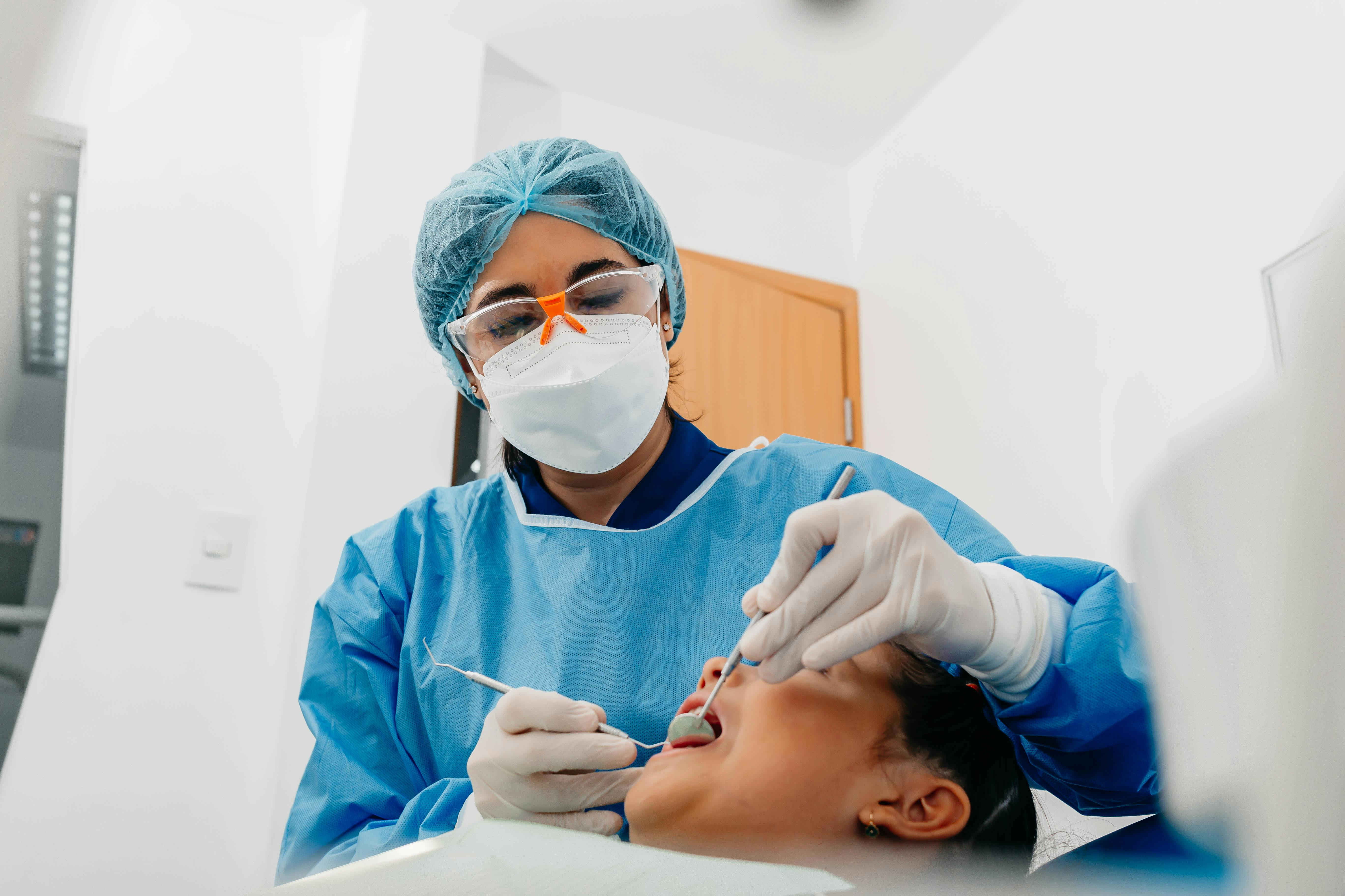 Healthcare worker in blue scrubs adjusting gloves in clinical setting with green curtains and equipment