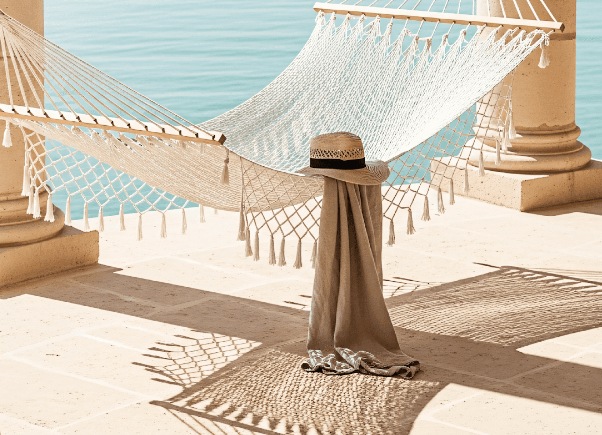 White hammock by the sea, casting shadows on stone floor, with hat and draped cloth.