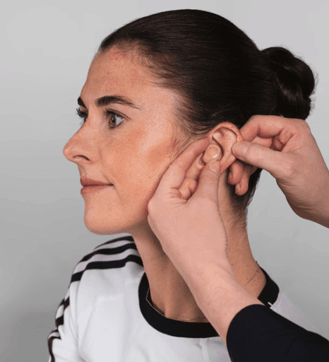 A person with a ponytail is getting their ear adjusted by someone off-screen. They are both focused on the task.