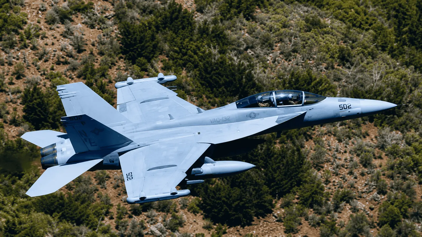 Military jet flying low over wooded hills during flight testing