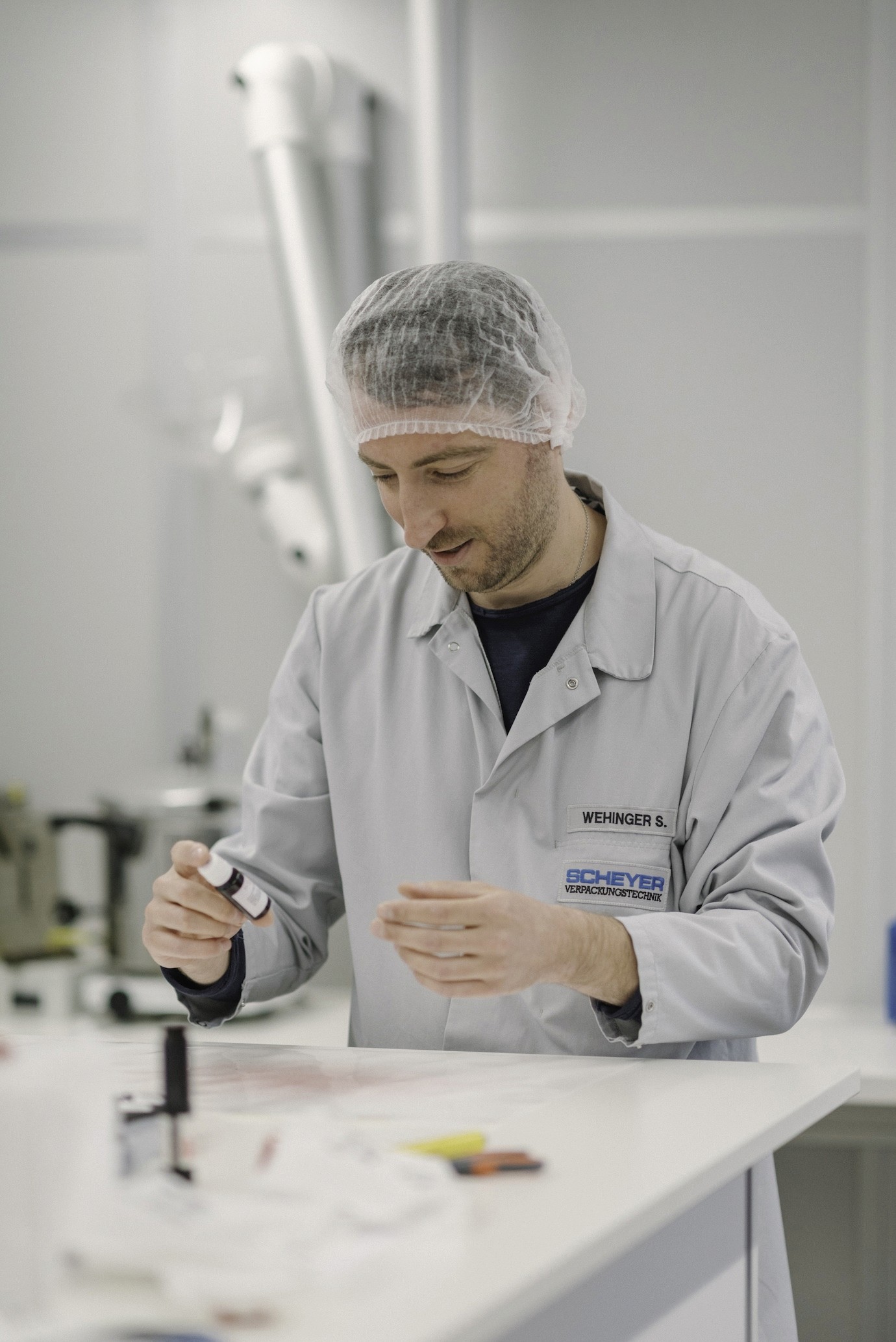 Technician at Scheyer handling a small bottle in a controlled environment.