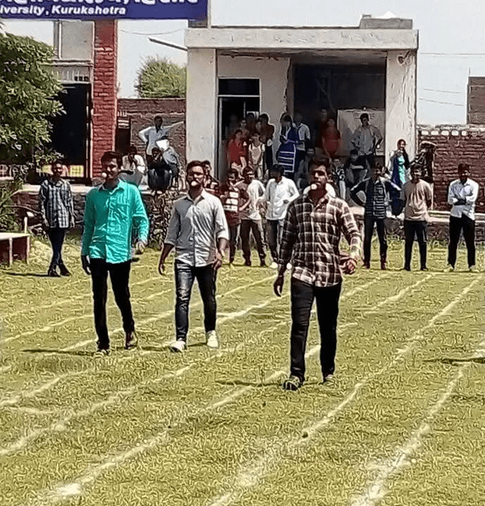 Male students competing in a college sports day race on a grassy campus field.