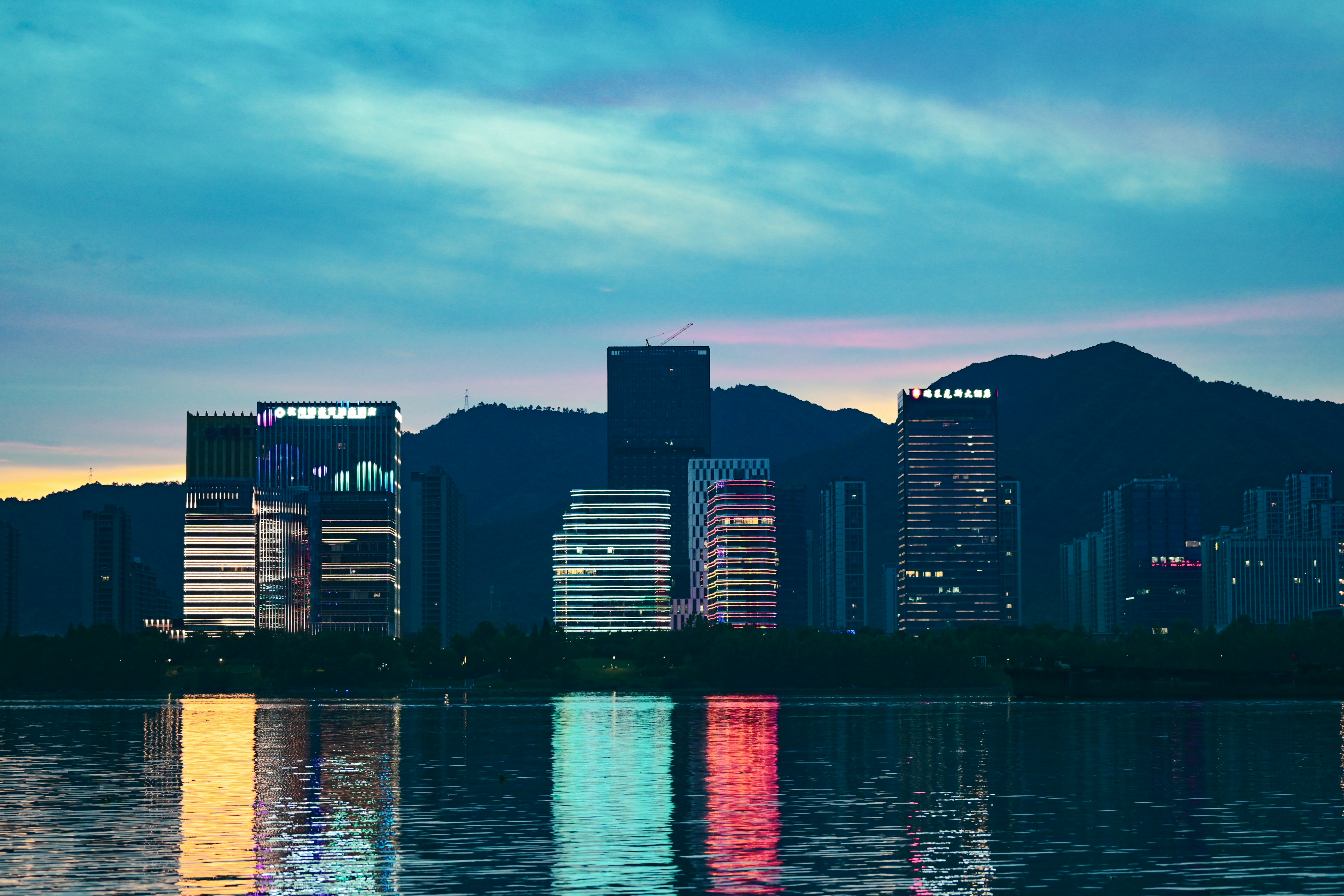 Buildings lit up at night next to waterfront which reflects the light further. 