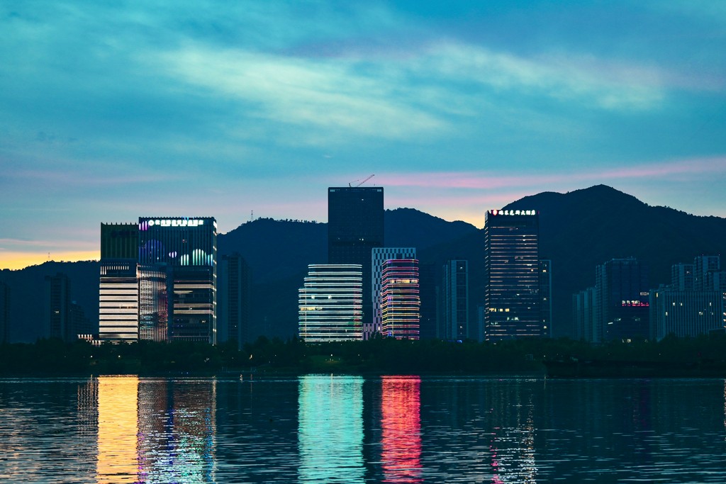 Buildings lit up at night next to waterfront which reflects the light further. 