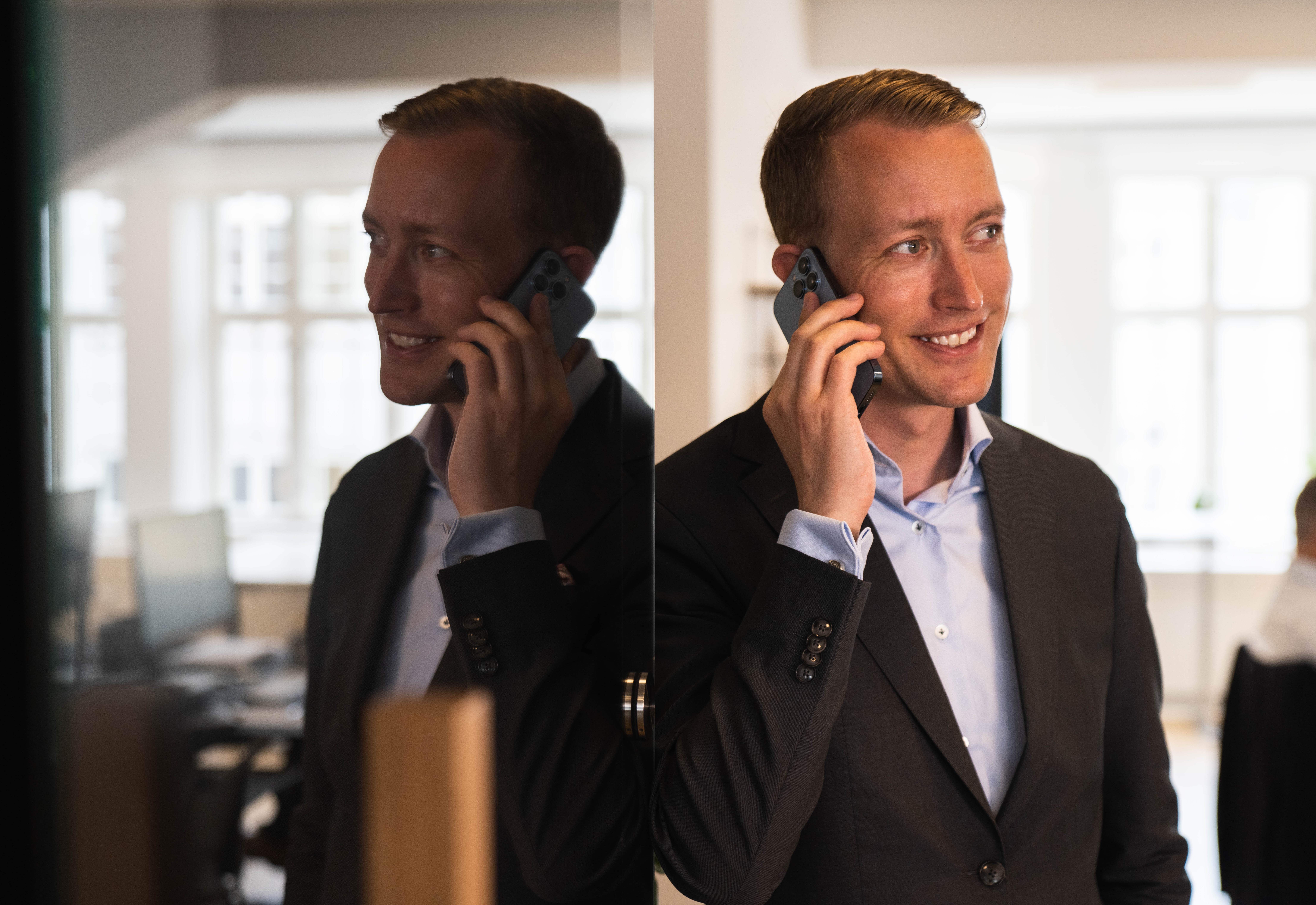 Smiling man in a maroon sweater working at a computer in a modern, industrial-looking lab or tech workspace.